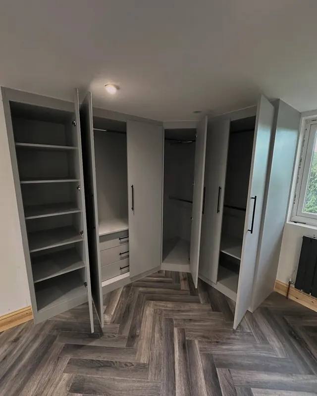 Grey corner wardrobes open, showing rails and drawers