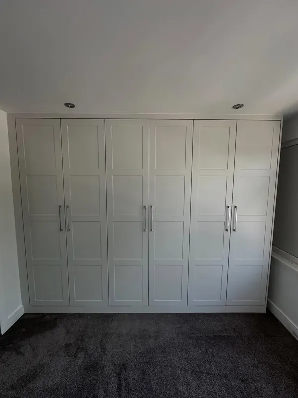 Cream fitted wardrobes with panelled doors across a bedroom wall