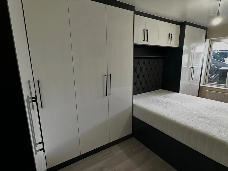 White gloss wardrobes fitted around a bed with a padded headboard