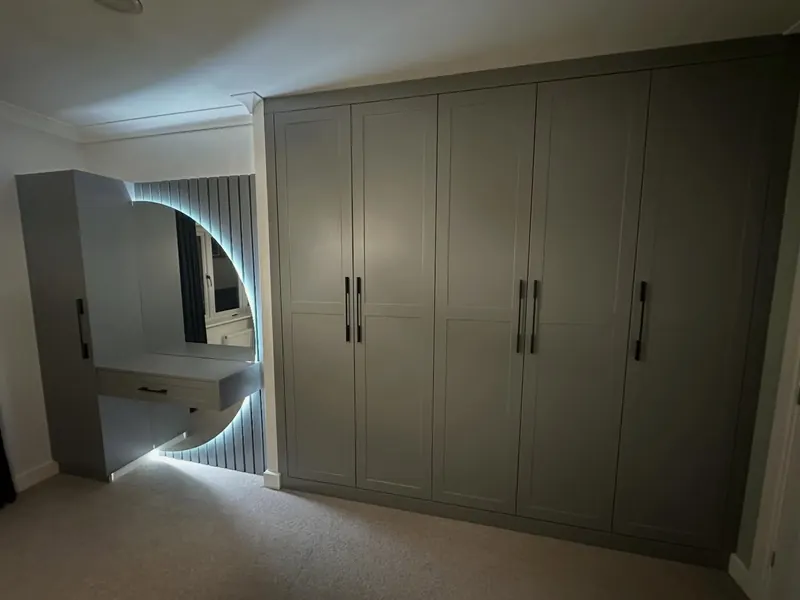 Sage green fitted wardrobes with a curved lit mirror and dressing table