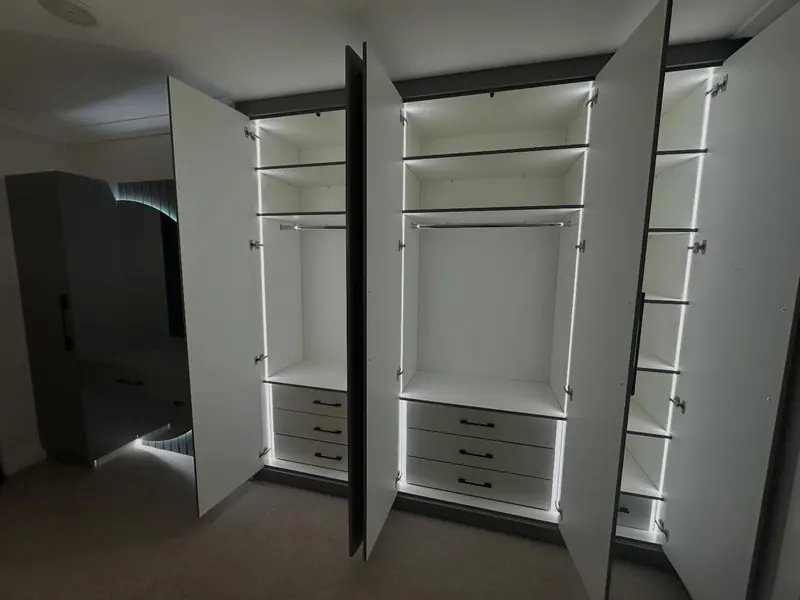 Sage green wardrobes open with LED strips lighting the shelves